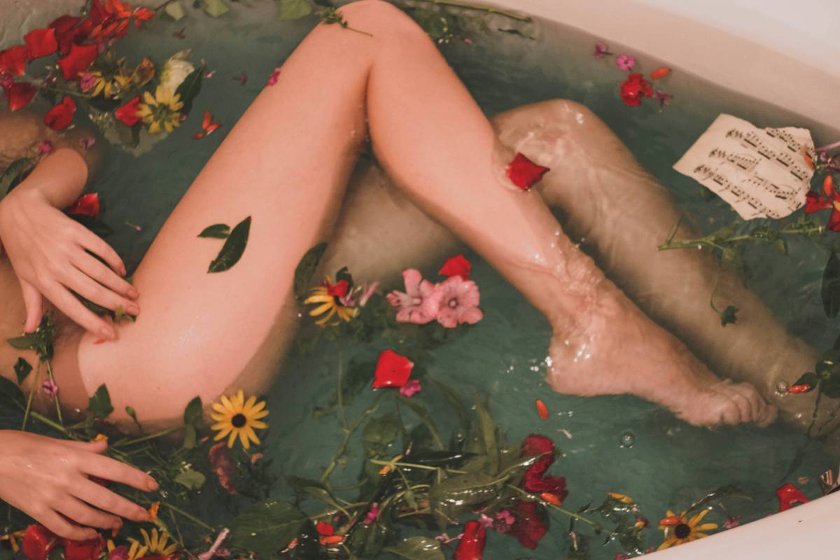 Woman applying bath and body aromatherapy lotion to her arms after a shower, surrounded by calming eucalyptus and lavender bottles